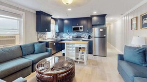 A modern kitchen with dark cabinetry, a central island, and a dining area. - Homey, comfortable condo w/ a furnished balcony - just blocks from the beach (Ocean City)