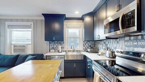 A modern kitchen with dark cabinetry, stainless steel appliances, and a wooden dining table. - Homey, comfortable condo w/ a furnished balcony - just blocks from the beach (Ocean City)