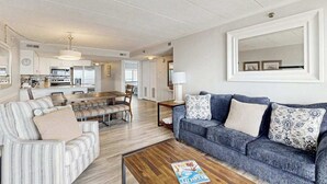 A modern living room with a sofa, a coffee table, and a dining area with chairs and a table. - Beachy Getaway Steps From Water w/Shared Pool, WiFi, AC, & Private Washer/Dryer (Ocean City)