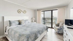 A bedroom with a bed, a TV, a dresser, and a balcony with a view. - Beachy Getaway Steps From Water w/Shared Pool, WiFi, AC, & Private Washer/Dryer (Ocean City)