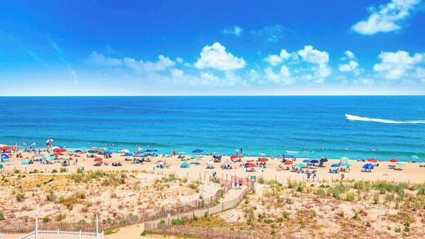 A beach with umbrellas and people, a clear sky, and a boat in the water. - Beachy Getaway Steps From Water w/Shared Pool, WiFi, AC, & Private Washer/Dryer (Ocean City)