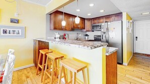 A kitchen with wooden cabinets, a granite countertop, and a stainless steel refrigerator. - Oceanfront Mooring Condo w/ Ocean View, WiFi, W/D, AC - Relax and Unwind (Ocean City)