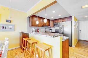 A kitchen with wooden cabinets, a granite countertop, and a stainless steel refrigerator. - Oceanfront Mooring Condo w/ Ocean View, WiFi, W/D, AC - Relax and Unwind (Ocean City)