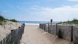 A sandy beach path leading to the ocean, bordered by wooden fences and dunes.