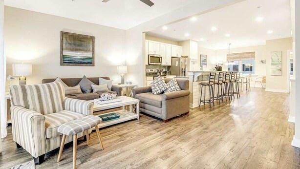 A spacious living area with a sofa, armchair, and coffee table, a kitchen in the background, and a ceiling fan. - Seaside Village - Bowline 13002-4 (West Ocean City)