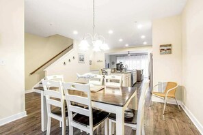 A dining area with a wooden table and white chairs, a staircase, and a kitchen in the background. - Seaside Village - Bowline 13002-4 (West Ocean City)