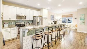 A modern kitchen with white cabinets, a central island with bar stools, stainless steel appliances, and a green-tiled backsplash. - Seaside Village - Bowline 13002-4 (West Ocean City)