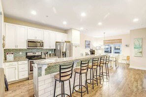 A modern kitchen with white cabinets, a central island with bar stools, stainless steel appliances, and a green-tiled backsplash. - Seaside Village - Bowline 13002-4 (West Ocean City)