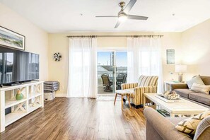A living room with a flat-screen TV, a ceiling fan, a sofa, a coffee table, and a view through a glass door. - Seaside Village - Bowline 13002-4 (West Ocean City)