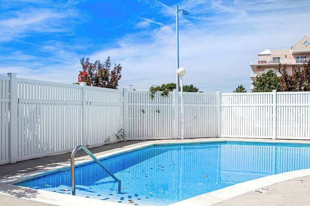 Une piscine entourée d’une clôture blanche, avec une échelle en métal et un lampadaire.