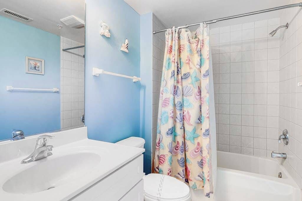 Ein Badezimmer mit Badewanne, einer Duschkabine mit Blumenmuster, einem weißen Waschbecken und einem Spiegel.