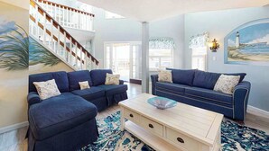 Ein geräumiges Wohnzimmer mit Treppe, blauen Sofas, einem Couchtisch und einem Gemälde eines Leuchtturms.