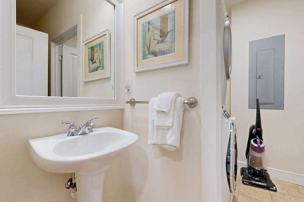Un baño con lavamanos, espejo, toallero y una aspiradora.