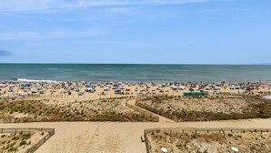Een strand met veel parasols en mensen, zand en een heldere lucht.