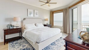 Een slaapkamer met een groot bed, nachtkastjes, een plafondventilator en uitzicht op de oceaan.