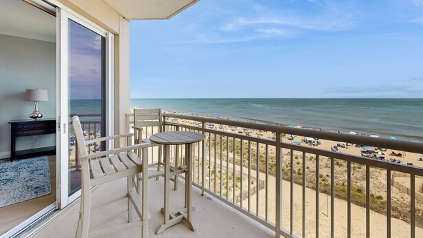 Een balkon met uitzicht op het strand, een tafel, een stoel en een lamp.