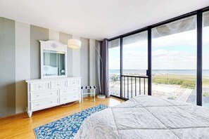 A bedroom with a large bed, a dresser, a mirror, and a view of the beach through a balcony. - Oceanfront Century I Condo w/ Ocean & Bay Views, WiFi, AC, W/D, Shared Pool/Gym (Ocean City)