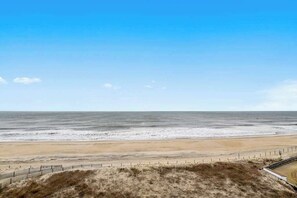 A beach with a fence and grassy area in the foreground. - Eastwinds 505 (Ocean City)