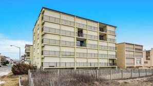 A multi-story building with balconies, a flat facade, and a wooden fence in front. - Eastwinds 505 (Ocean City)
