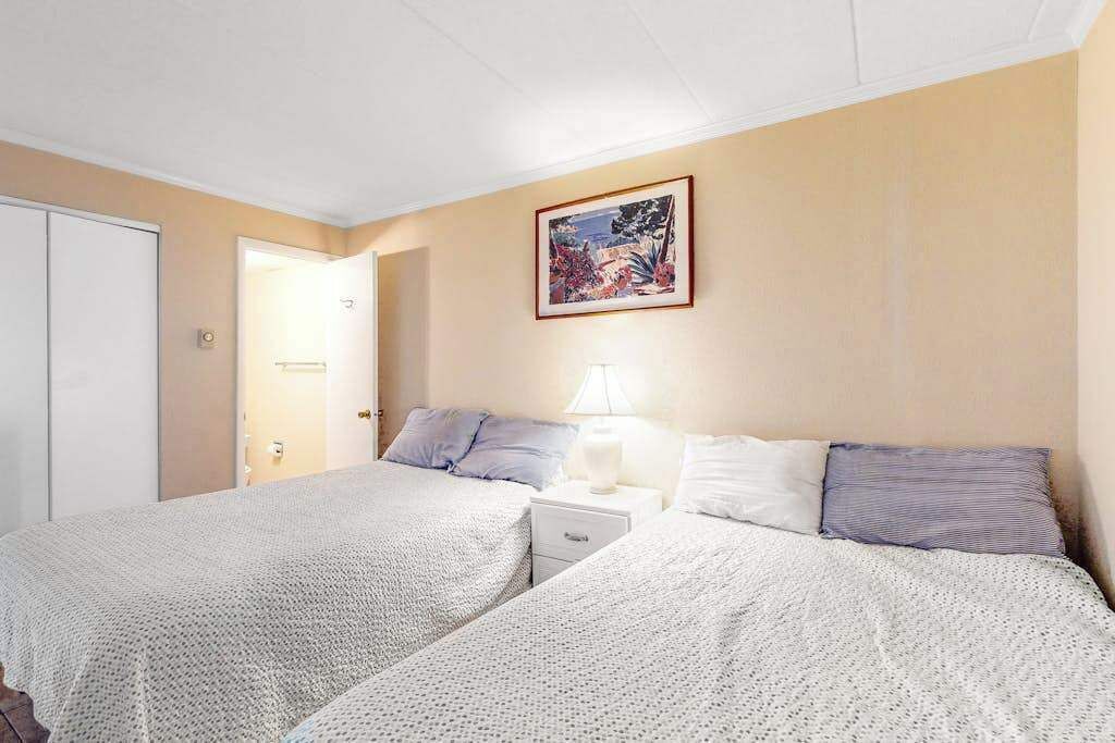 A bedroom with two beds, a nightstand, a bedside lamp, and a framed picture on the wall.