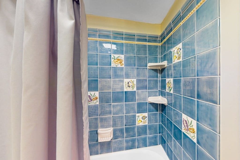 A bathroom with blue tiles, a white bathtub, and a towel rack.