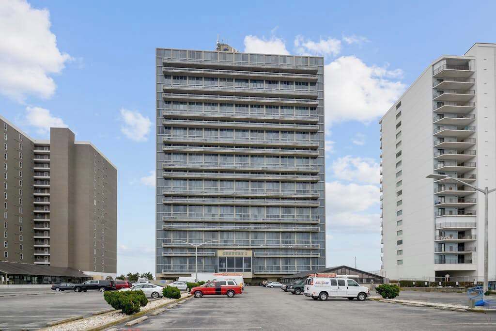 Een meerhoog gebouw met een modern architectonisch ontwerp, met een centrale ingang en een parkeerplaats ervoor.