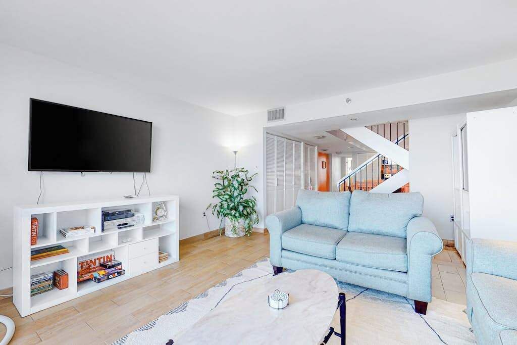 Un salon équipé d’un téléviseur à écran plat, d’un canapé bleu clair, d’un meuble de rangement blanc et d’un escalier menant à un autre niveau.