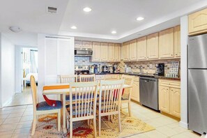 A modern kitchen with wooden cabinets, stainless steel appliances, and a dining area with a table and chairs. - Oceanfront Century I Condo w/ Ocean View, WiFi, Washer/Dryer, AC, Shared Pool (Ocean City)