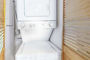 A compact, white laundry room with a built-in washer and dryer, enclosed by wooden paneling. - Oceanfront Century I Condo w/ Ocean View, WiFi, Washer/Dryer, AC, Shared Pool (Ocean City)