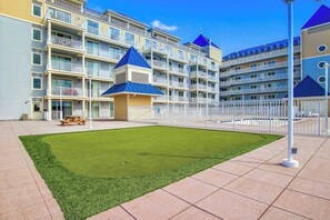 A multi-story hotel with balconies, a central courtyard with artificial grass, and a white fence. - Belmont Towers 301 (Ocean City)