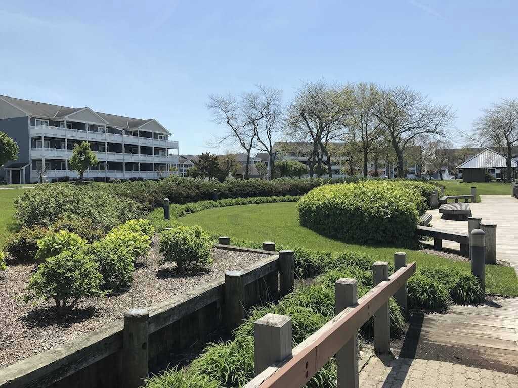 A multi-story building with a flat roof, surrounded by well-maintained gardens and a wooden fence.