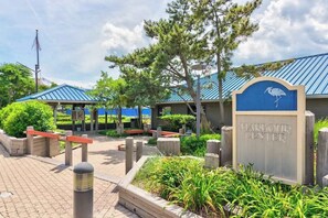 A sign for the Harbour Center with a blue roof, surrounded by greenery and wooden benches. - Heron Haven (Ocean City)