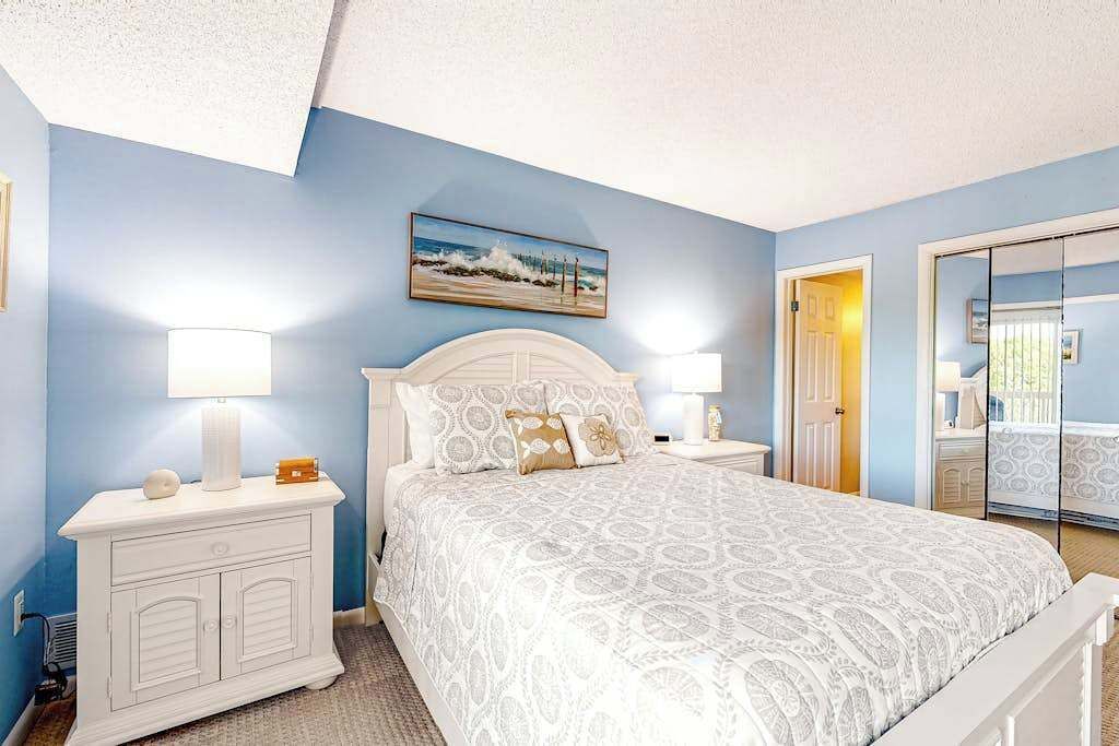 Une chambre à coucher comprenant un lit, des tables de chevet, une commode, un tableau et une porte donnant sur une autre pièce.