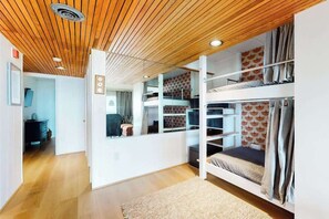 A bunk bed room with a wooden ceiling, a white wall with a geometric pattern, and a visible door leading to another room. - Beachloft 2G (Ocean City)