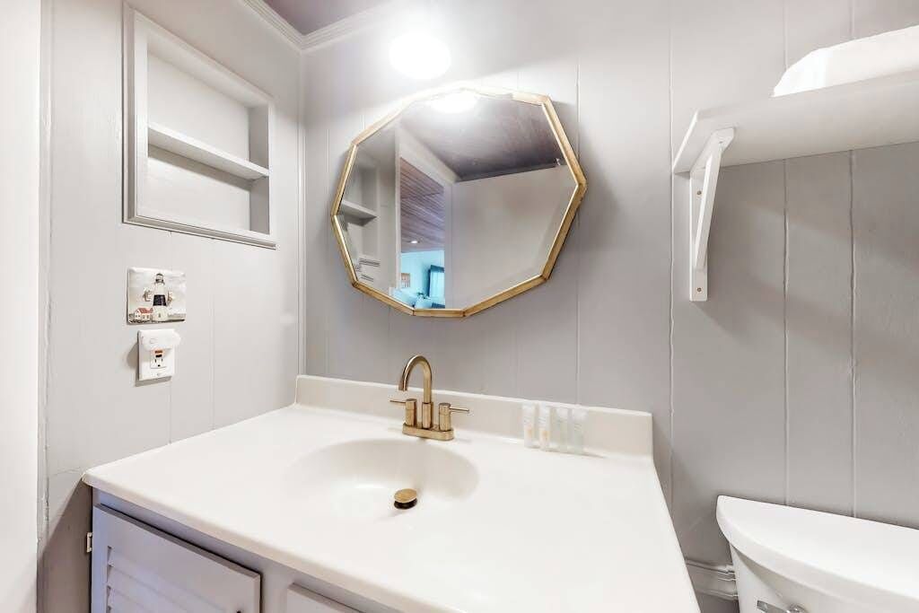 A bathroom with a white sink, gold faucet, and a large octagonal mirror.