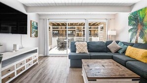 En stue med sofa, sofabord, fjernsyn og en balkon med udsigt.