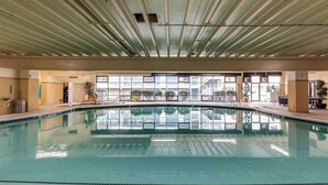 Ein überdachter Schwimmbereich mit großen Glaswänden, einer Metalldecke und Blick auf die umliegenden Gebäude.