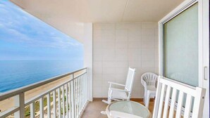 Ein Balkon mit Meerblick, weißen Korbstühlen und einer Glastür.