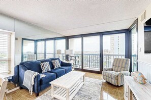 Ein geräumiger Balkon mit einem blauen Sofa, einem gestreiften Sessel und einem Holztisch.