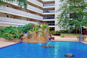 Ein Hotel mit Schwimmbad, einem Wasserfall aus Stein und einem mehrstöckigen Gebäude mit Balkonen.