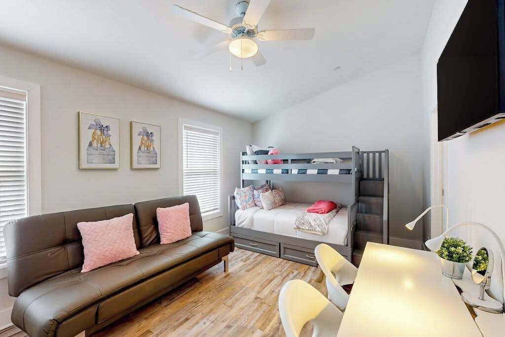 A compact room with a bunk bed, a sofa, a dining table, and a ceiling fan.