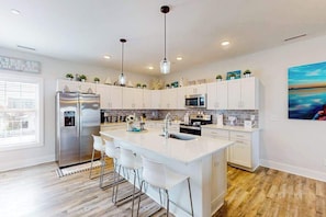 A modern kitchen with a central island, stainless steel appliances, and pendant lighting. - Upscale canal-front townhome with pool, beach access, dock, balconies, & desks (Ocean City)