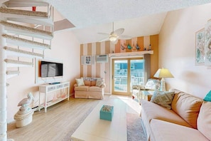 A living room with a TV, sofa, and a balcony with a view. - Waterfront townhome with pool - walk to the beach, boardwalk & Jolly Roger (Ocean City)