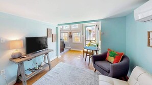 A living room with a television on a wooden stand, a sofa, a dining table, and a view into the kitchen. - Cottages on St Louis #2 (Ocean City)