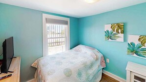 A bedroom with a bed, a TV on a stand, a window with blinds, and artwork on the wall. - Cottages on St Louis #2 (Ocean City)