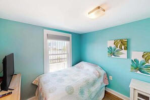 Ein Schlafzimmer mit einem Bett, einem Fernseher auf einem Schrank, einem Fenster mit Jalousien und Bildern an der Wand.