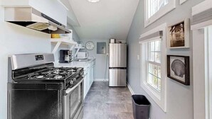 A modern kitchen with a stove, microwave, and refrigerator, a clock on the wall, and framed artwork on the wall. - Cottages on St Louis #2 (Ocean City)
