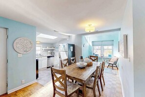 Eine moderne Küche mit weißen Schränken, ein Essbereich mit Holztisch und Stühlen, und eine hellblaue Wand.
