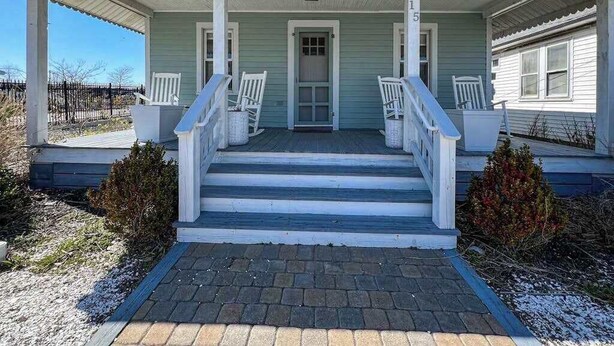 A porch with steps leading to a door, white railings, and two white chairs. - Cottages on St Louis #3 (Ocean City)