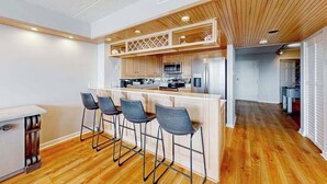Een moderne keuken met houten kasten, een centraal kookeiland met barkrukken, en een zichtbare magnetron en koelkast.